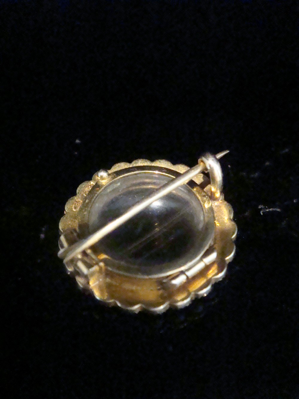 A circular Edwardian 9ct yellow gold locket brooch set with a perimeter halo of seed pearls framing a central glazed glass compartment. View III