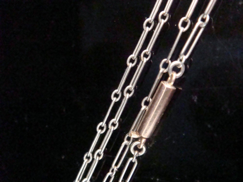 Close-up of a delicate Edwardian platinum trombone and paperclip link chain against a dark background.