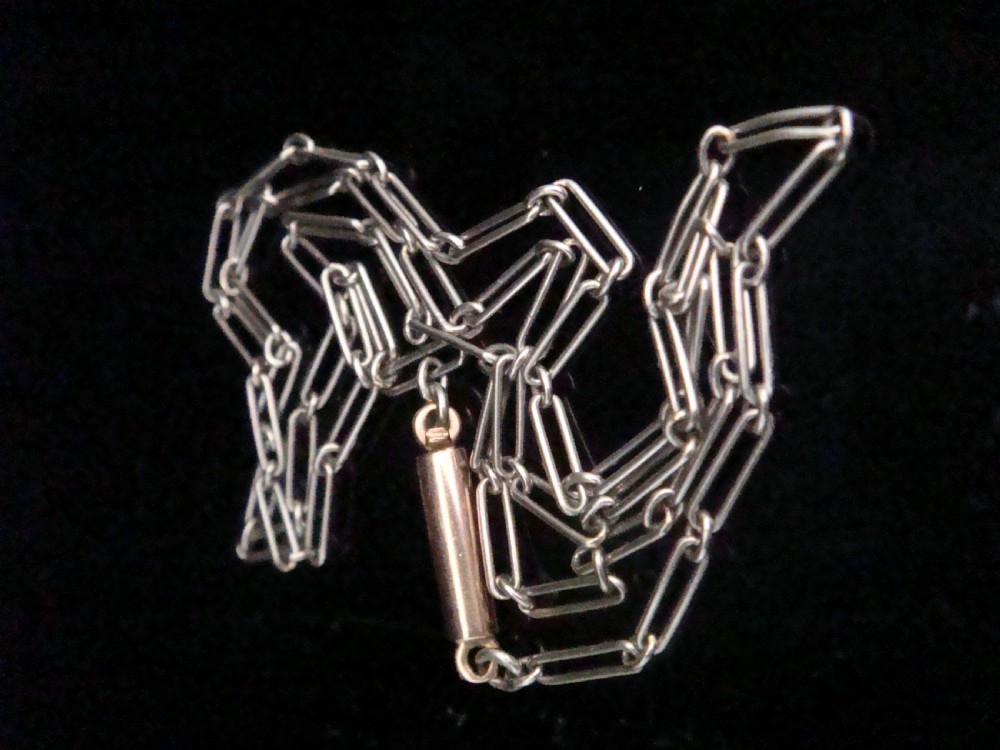Close-up of a delicate Edwardian platinum trombone and paperclip link chain against a dark background. View II