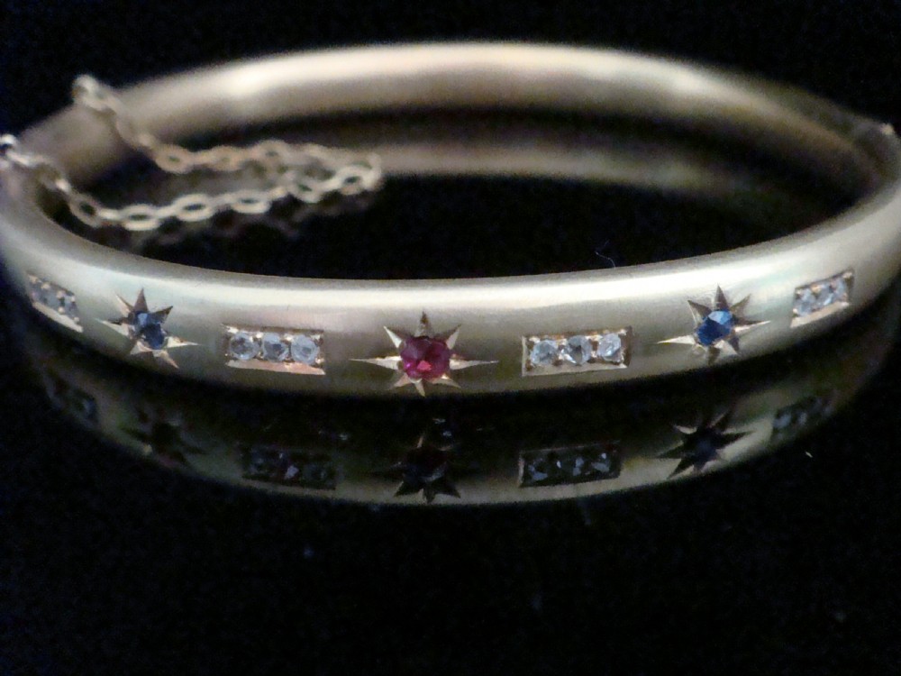 A matte 15ct yellow gold hinged bangle featuring star-set sapphires and rubies alongside rose-cut diamond accents.