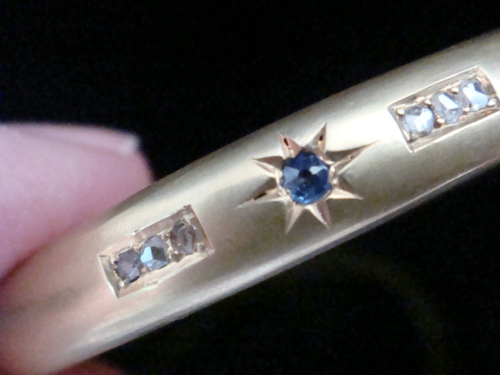 A matte 15ct yellow gold hinged bangle featuring star-set sapphires and rubies alongside rose-cut diamond accents. View IV