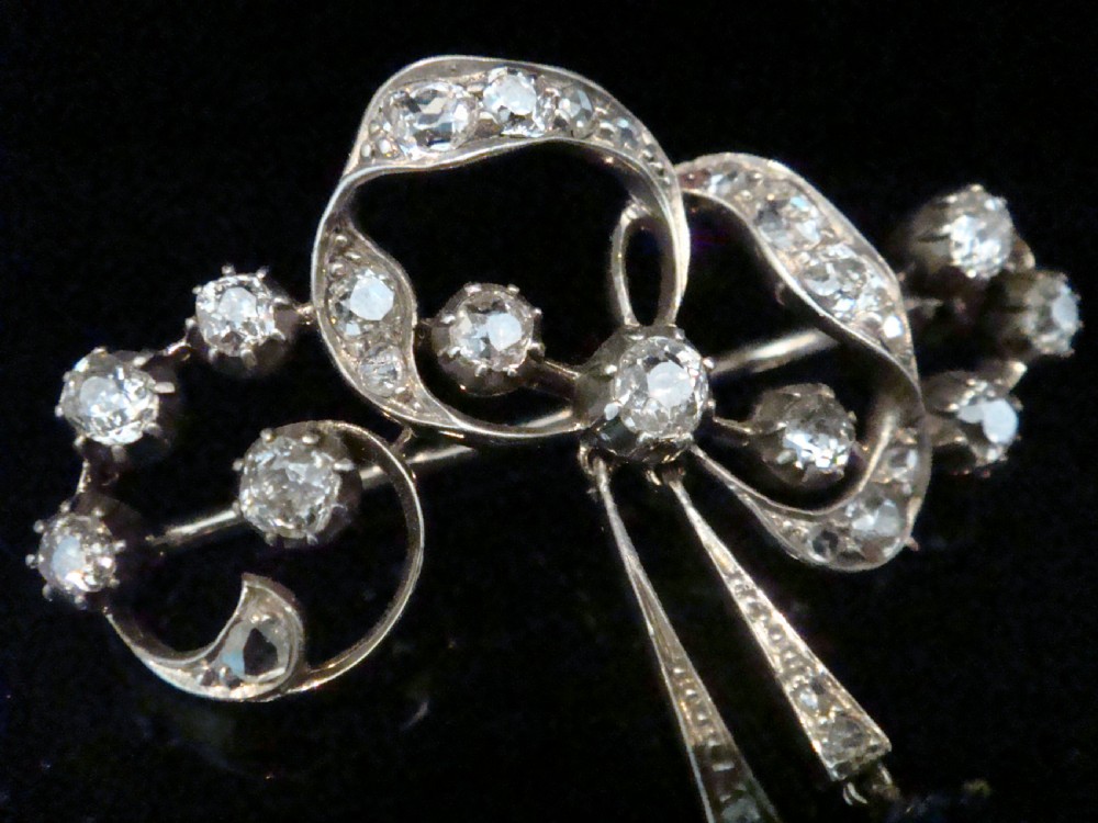 An Edwardian silver and gold bow brooch set with round diamonds and two hanging oval blue sapphires. View II