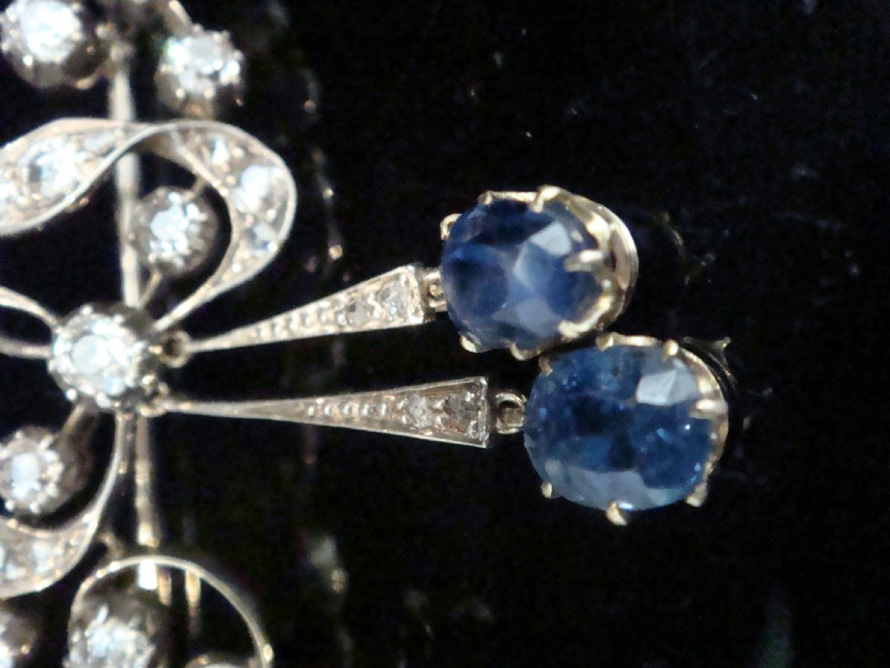 An Edwardian silver and gold bow brooch set with round diamonds and two hanging oval blue sapphires. View III