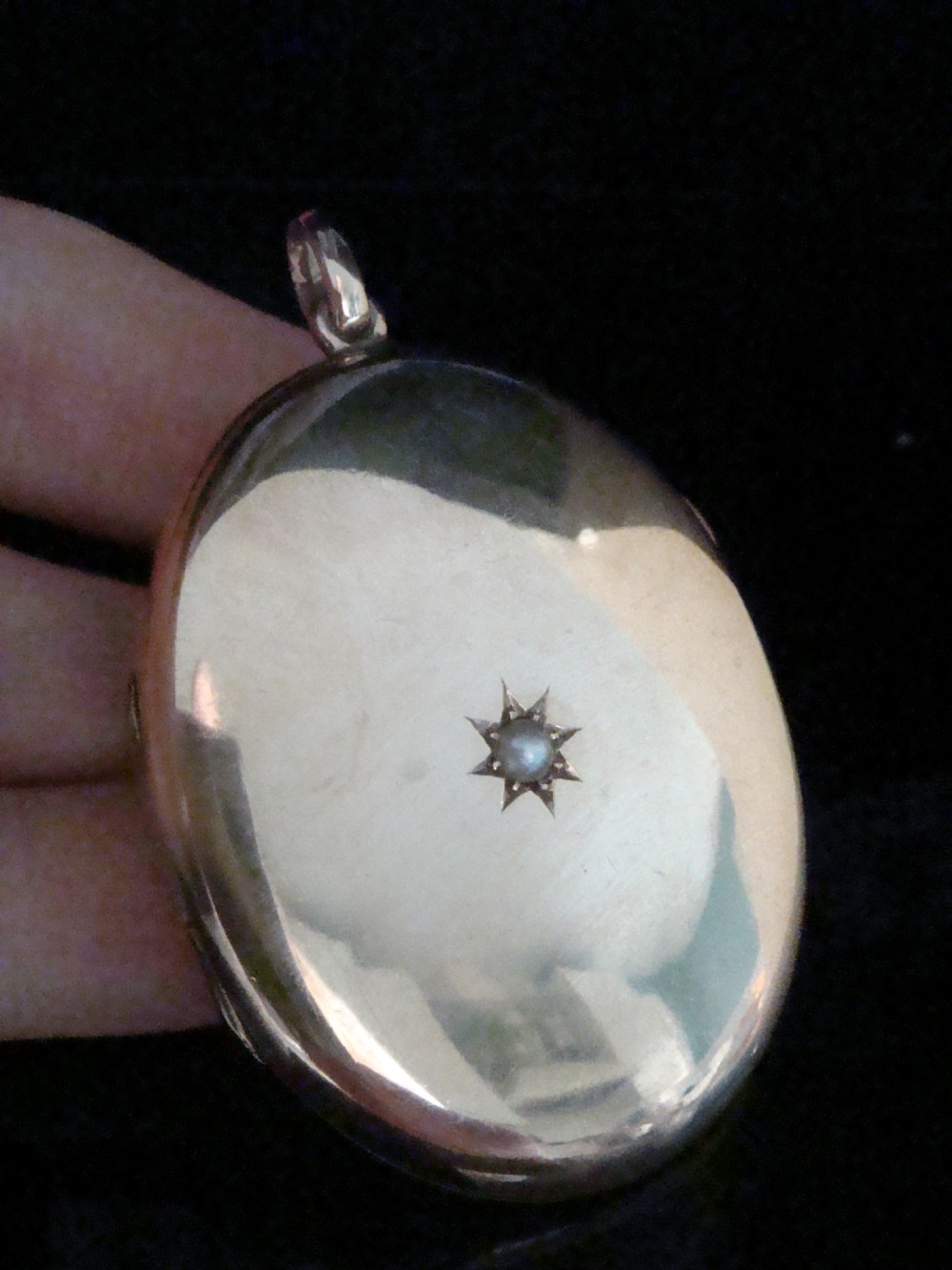An oval 9ct rose gold Edwardian locket featuring a centrally inset starburst motif with a single seed pearl.