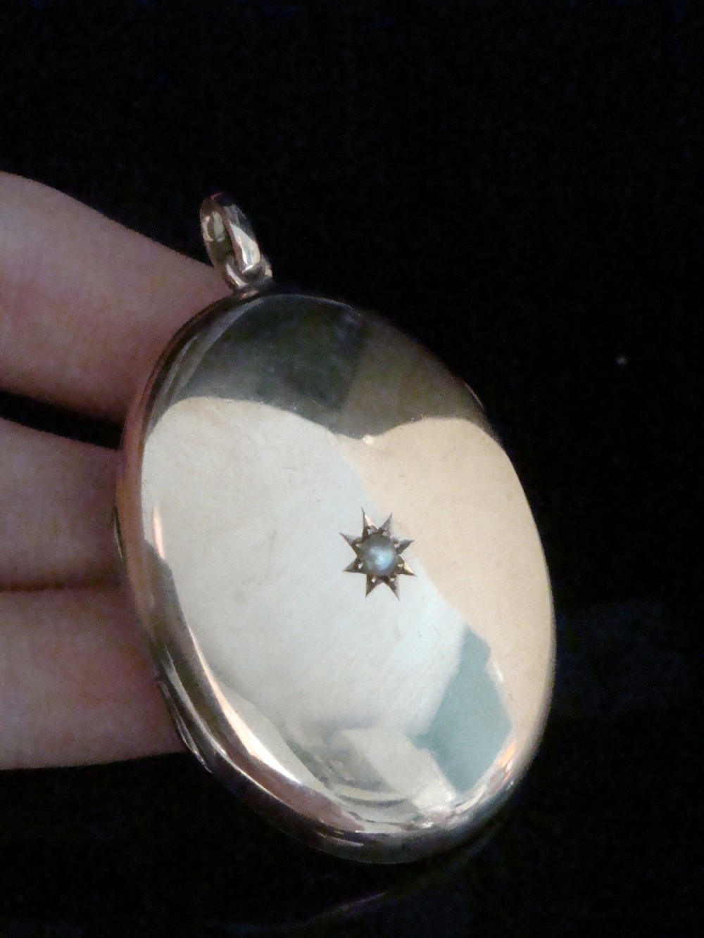 An oval 9ct rose gold Edwardian locket featuring a centrally inset starburst motif with a single seed pearl. View II