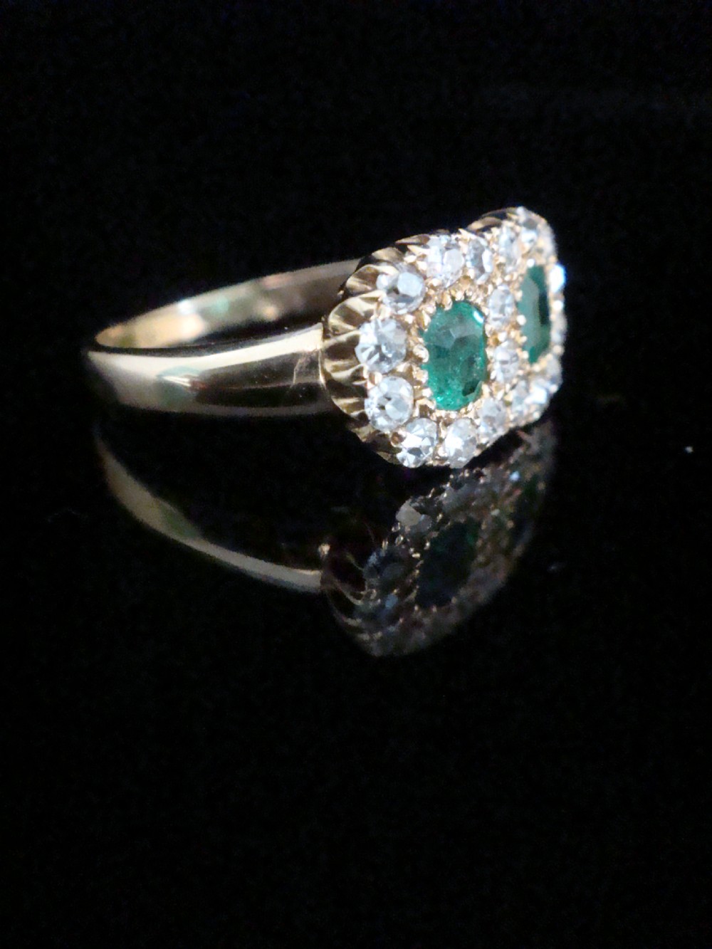 An Edwardian 18ct yellow gold ring featuring two central oval emeralds surrounded by a double cluster halo of diamonds. View II