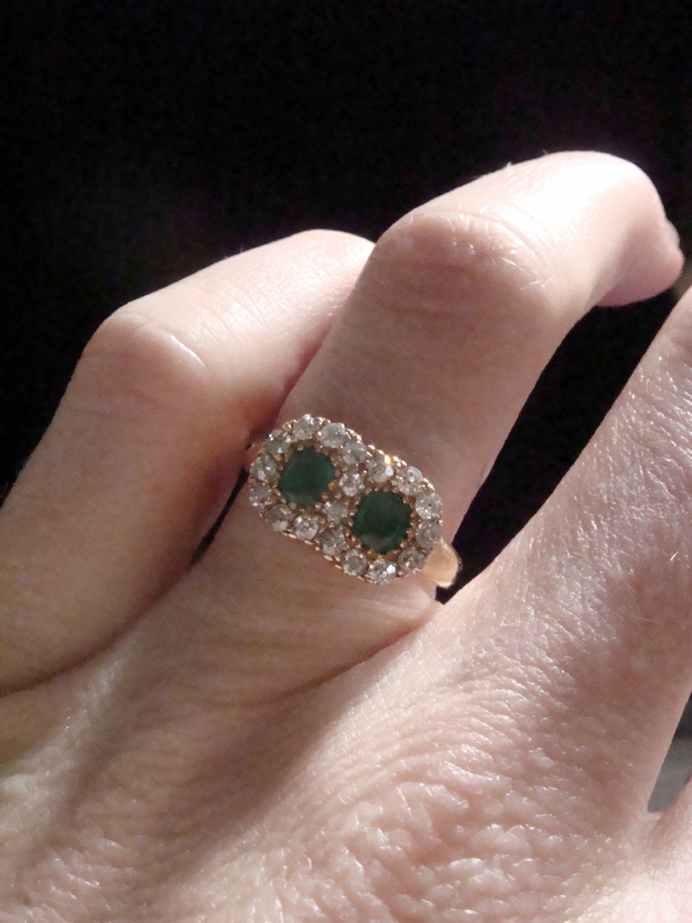 An Edwardian 18ct yellow gold ring featuring two central oval emeralds surrounded by a double cluster halo of diamonds. View III