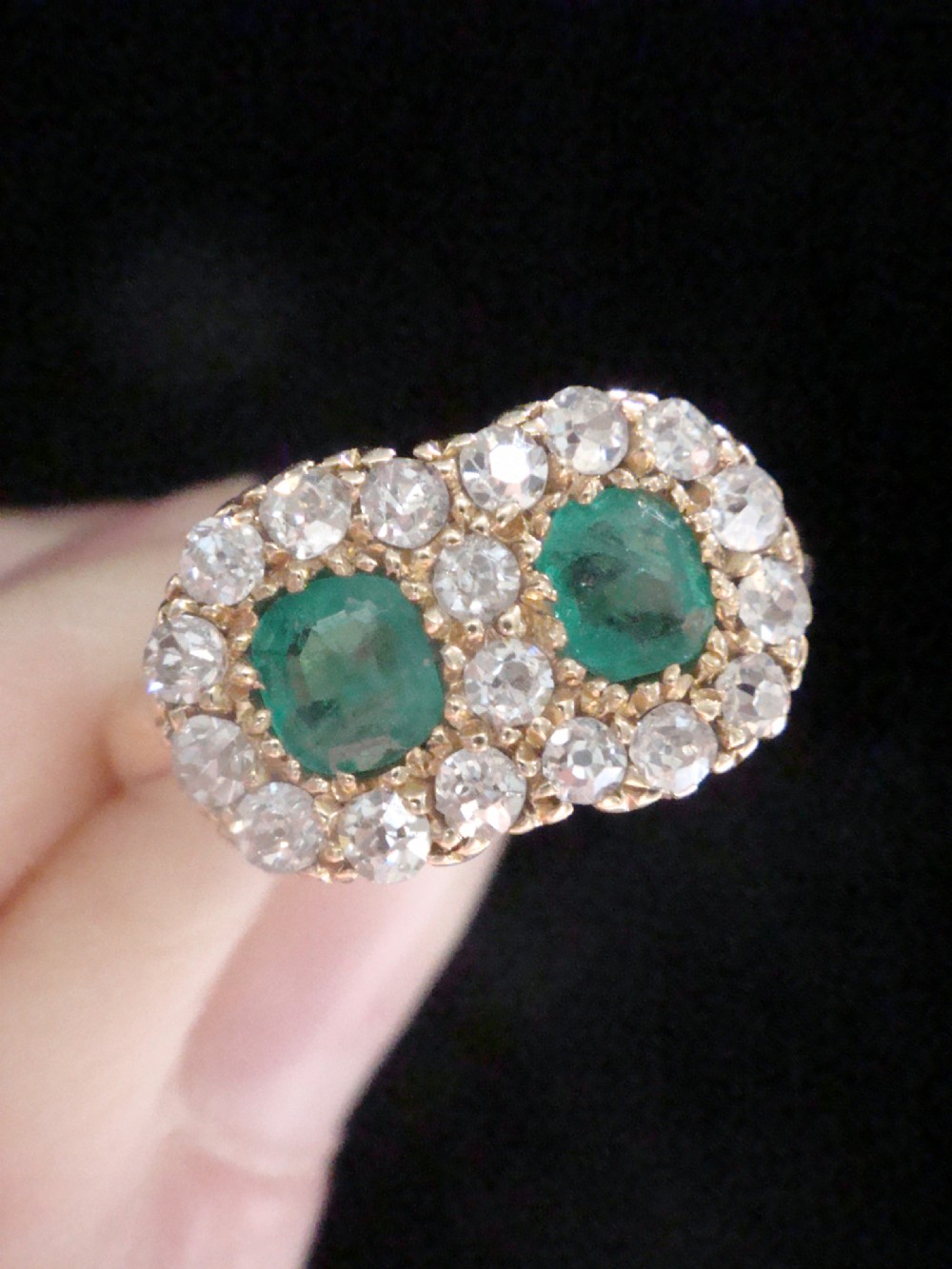 An Edwardian 18ct yellow gold ring featuring two central oval emeralds surrounded by a double cluster halo of diamonds. View VI