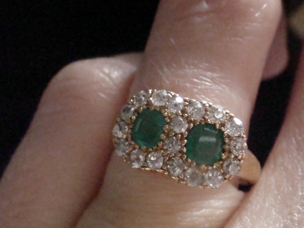 An Edwardian 18ct yellow gold ring featuring two central oval emeralds surrounded by a double cluster halo of diamonds. View VII