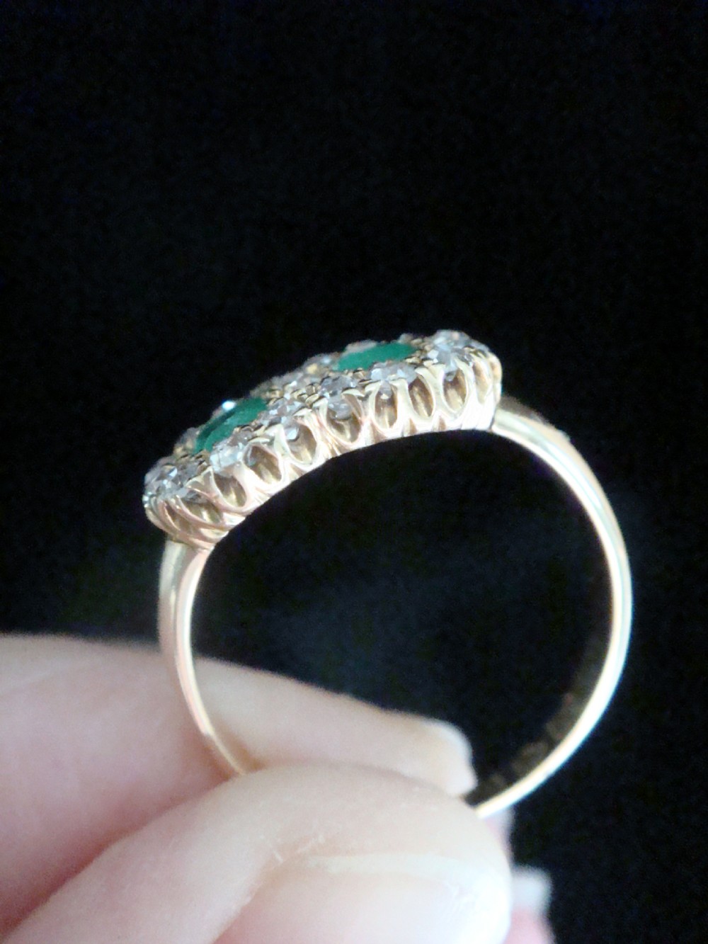 An Edwardian 18ct yellow gold ring featuring two central oval emeralds surrounded by a double cluster halo of diamonds. View VIII