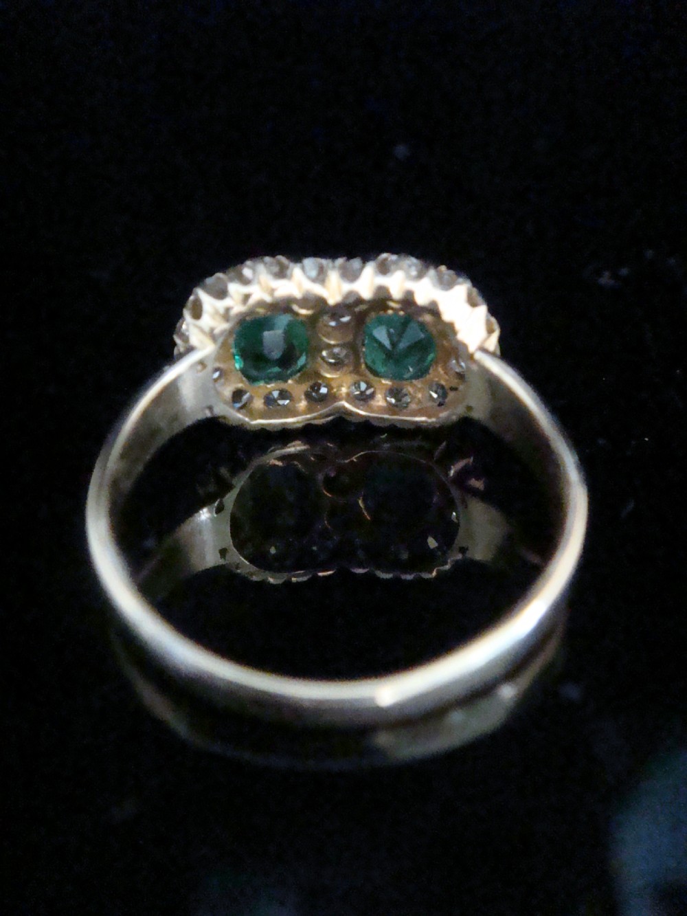 An Edwardian 18ct yellow gold ring featuring two central oval emeralds surrounded by a double cluster halo of diamonds. View IX
