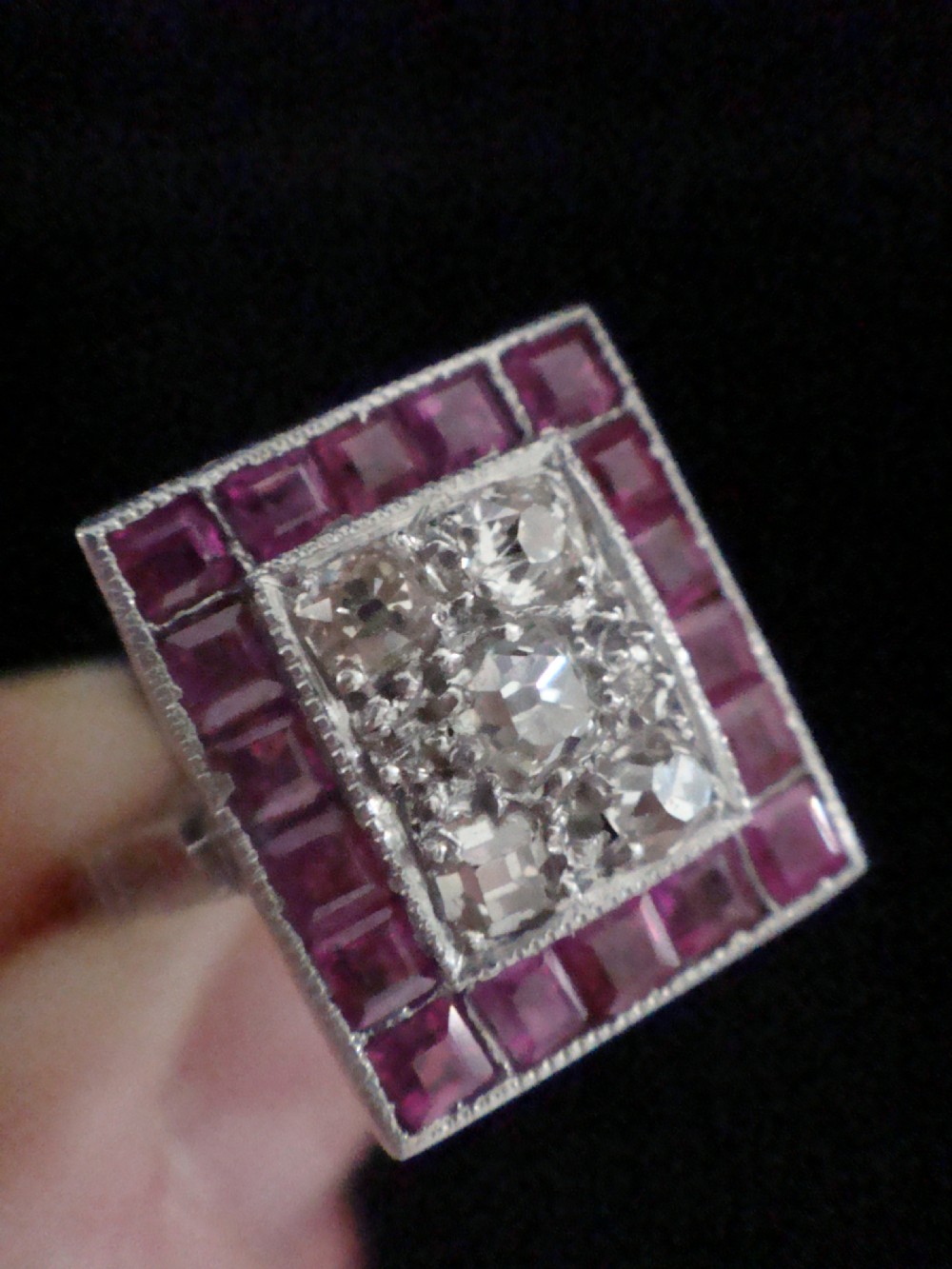 An Art Deco cluster ring featuring a central rectangular grid of round diamonds framed by square-cut natural rubies set in a white metal mount.