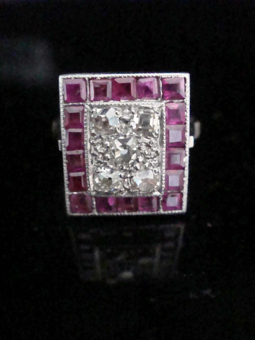 An Art Deco cluster ring featuring a central rectangular grid of round diamonds framed by square-cut natural rubies set in a white metal mount. View III