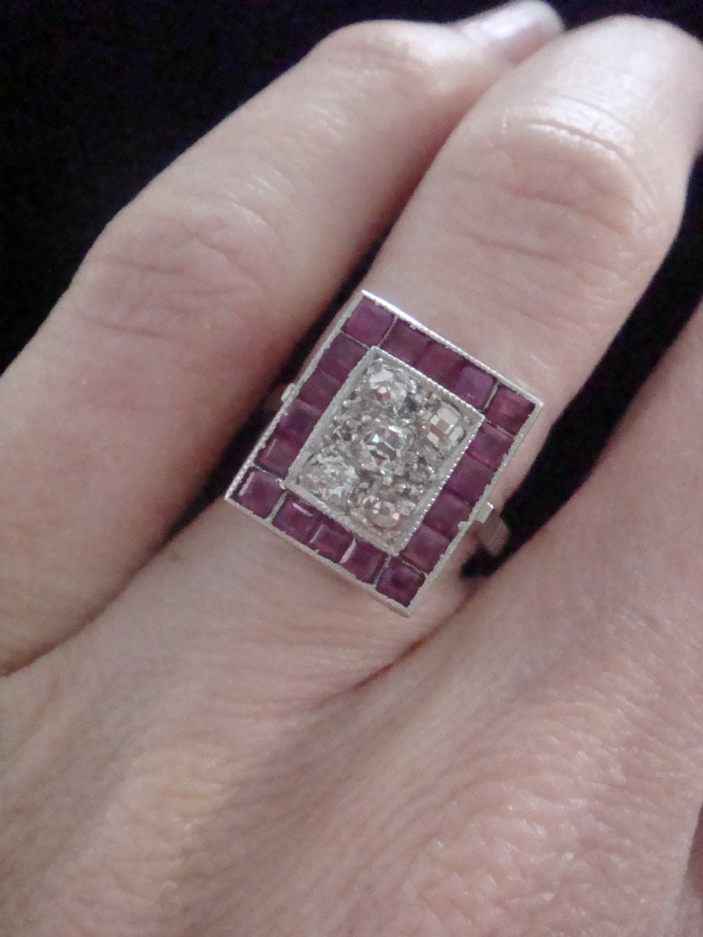 An Art Deco cluster ring featuring a central rectangular grid of round diamonds framed by square-cut natural rubies set in a white metal mount. View IV