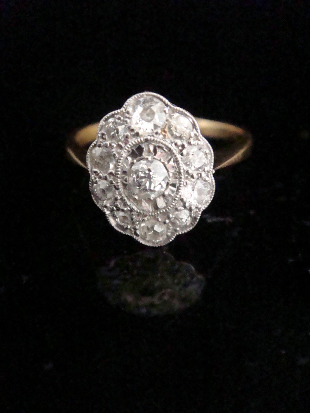 An Edwardian 18ct yellow gold and platinum ring featuring a scalloped cluster head pave-set with old cut diamonds and millegrain detailing.