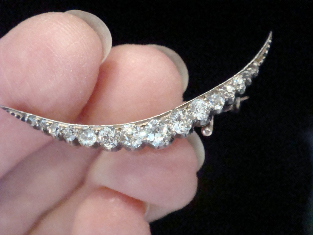 An Edwardian crescent moon brooch featuring a graduated row of round diamonds mounted in a curved precious metal setting with a pin back. View V