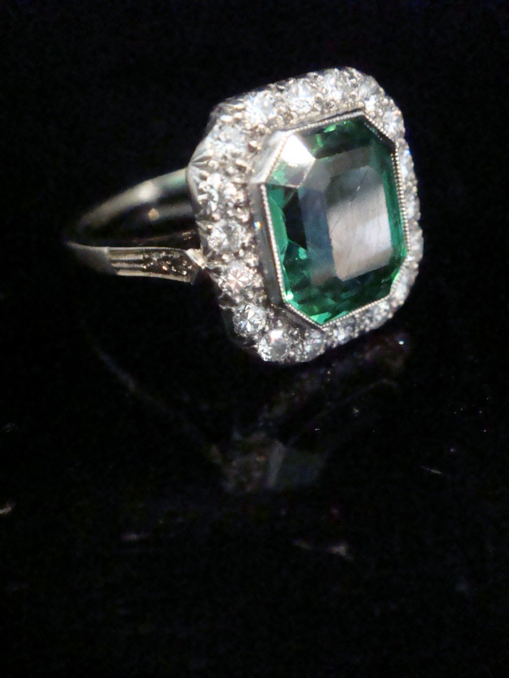 An Art Deco cluster ring featuring a central emerald-cut green tourmaline surrounded by a halo of diamonds set in platinum. View II