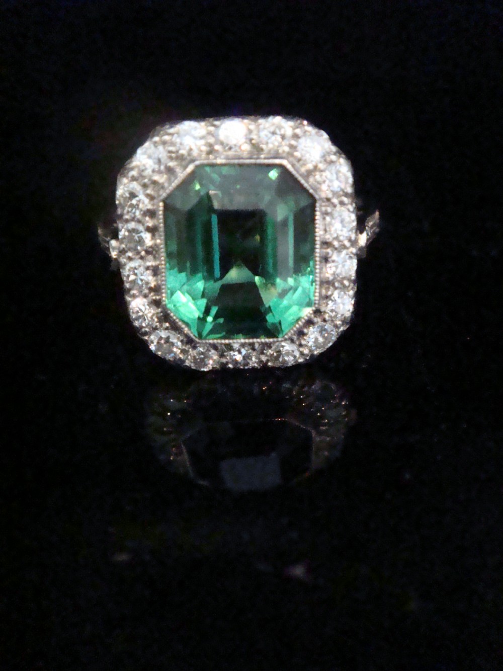 An Art Deco cluster ring featuring a central emerald-cut green tourmaline surrounded by a halo of diamonds set in platinum. View III