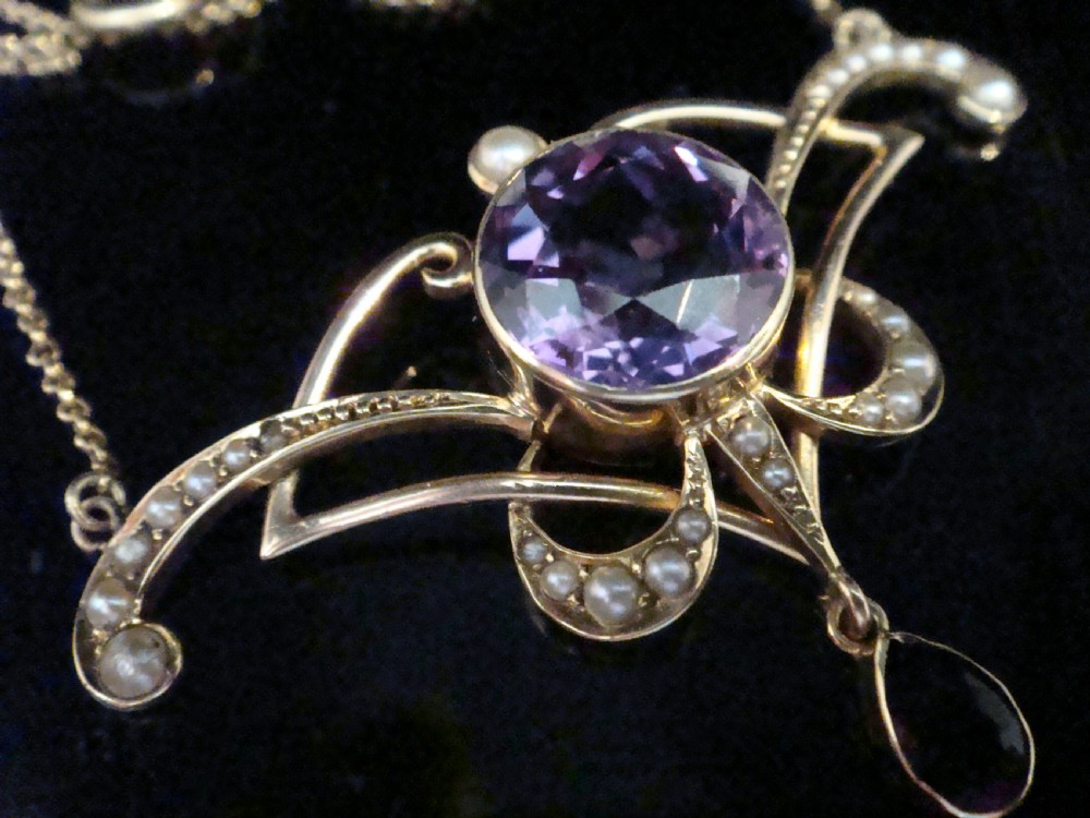 An Edwardian Art Nouveau 15ct gold lavaliere necklace featuring an openwork frame set with a round central amethyst, seed pearls, and a pear-cut dangling amethyst drop. View V