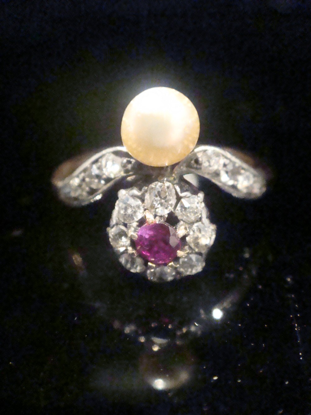 An Edwardian 18ct yellow gold ring featuring a central round ruby surrounded by old-cut diamonds with accent shoulder diamonds and a natural pearl. View II