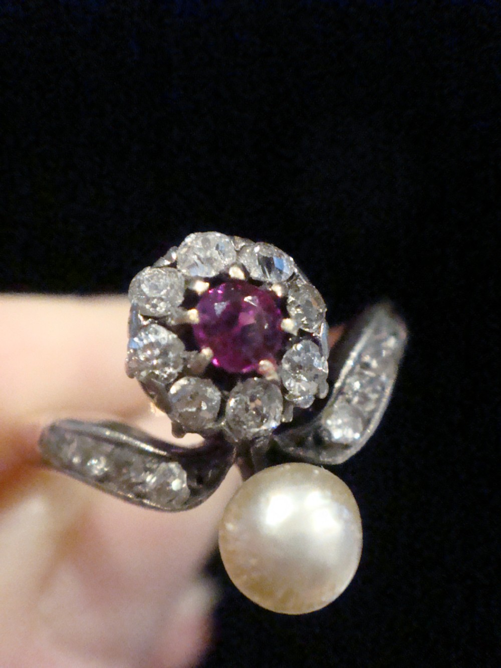 An Edwardian 18ct yellow gold ring featuring a central round ruby surrounded by old-cut diamonds with accent shoulder diamonds and a natural pearl. View VII