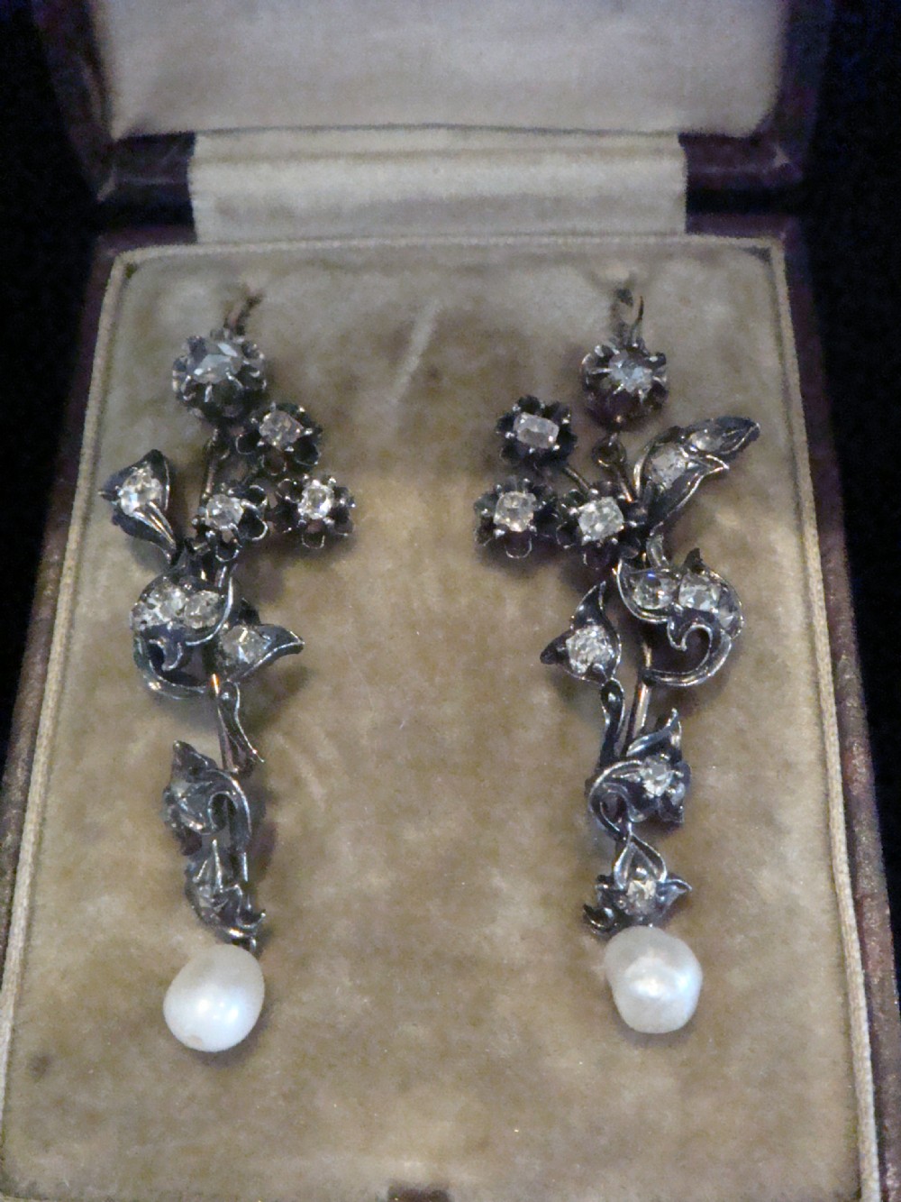 A pair of antique yellow gold and silver drop earrings featuring foliate diamond sprays and natural pearl drops presented inside a velvet box.