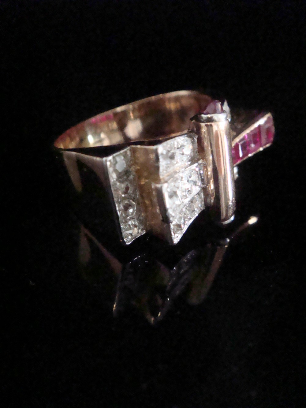 An 18ct gold Retro Modern tank ring featuring geometric diamond shoulders and a channel of calibre-cut red rubies. View II