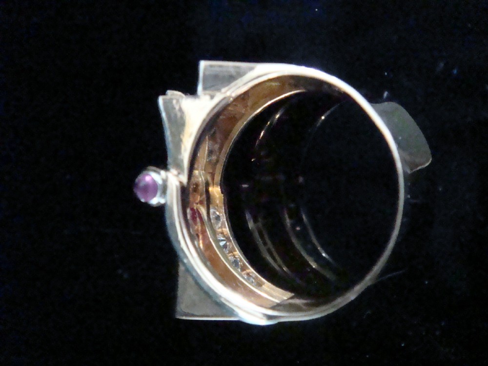 An 18ct gold Retro Modern tank ring featuring geometric diamond shoulders and a channel of calibre-cut red rubies. View IV