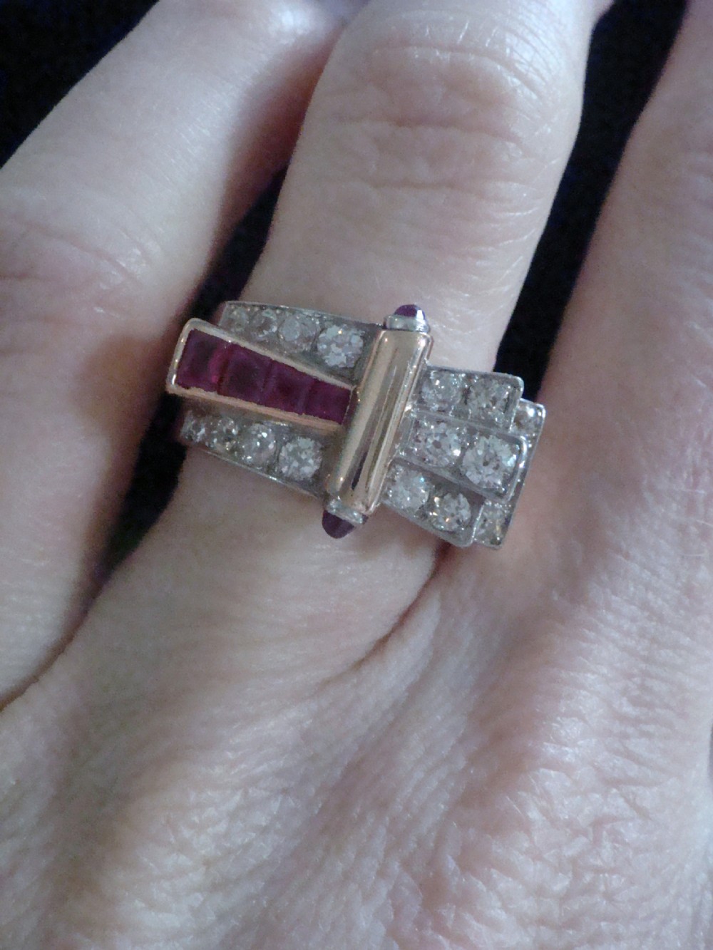An 18ct gold Retro Modern tank ring featuring geometric diamond shoulders and a channel of calibre-cut red rubies. View VI