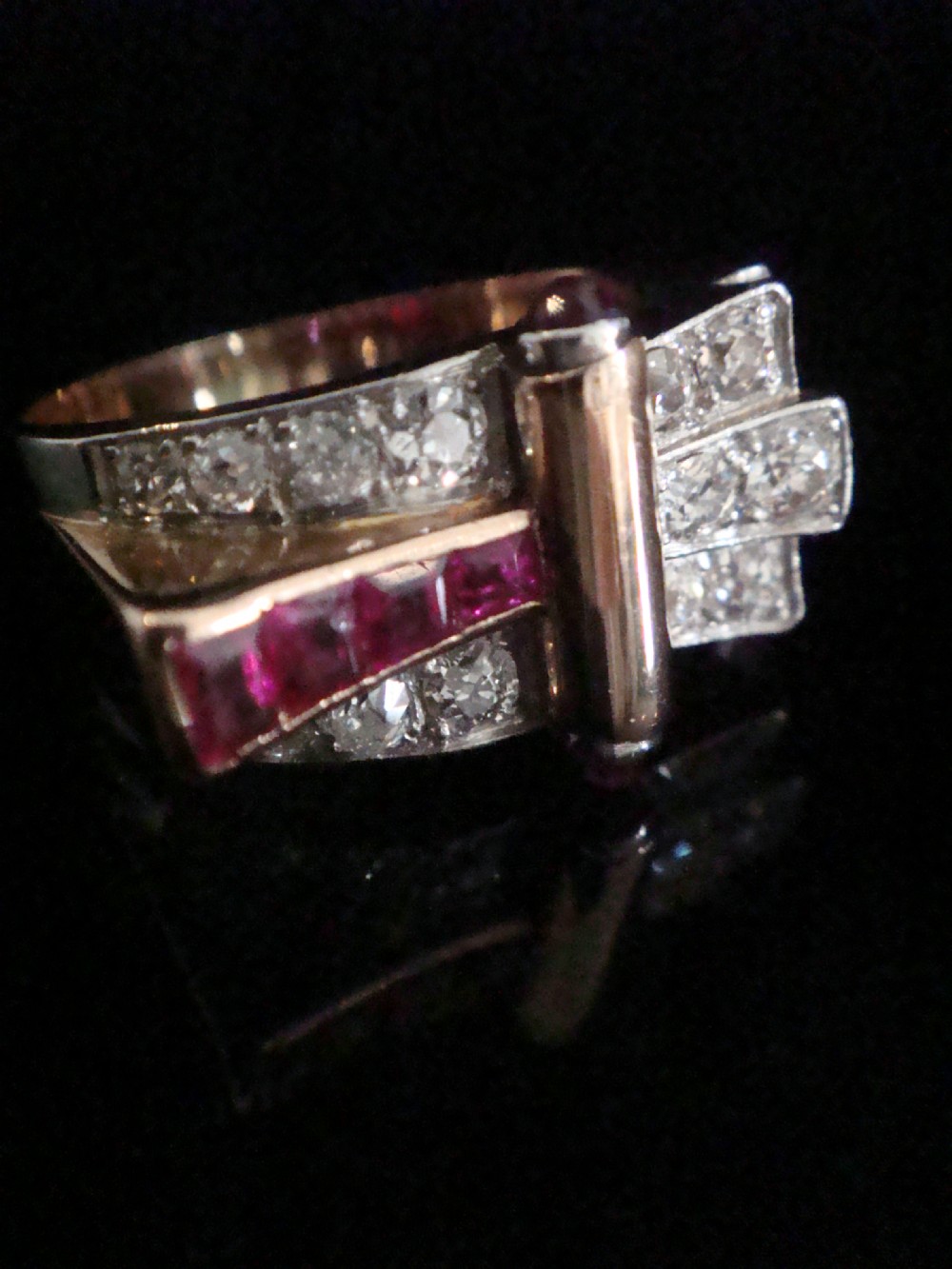 An 18ct gold Retro Modern tank ring featuring geometric diamond shoulders and a channel of calibre-cut red rubies. View X