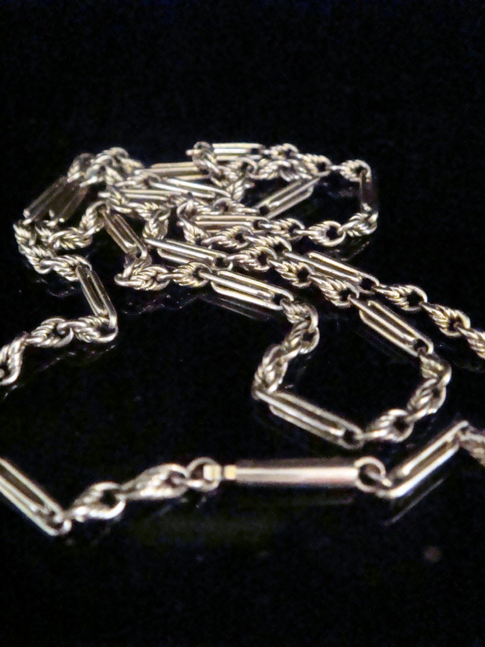 An Edwardian 9ct rose gold fetter and trombone link chain with a barrel clasp displayed on a dark surface.