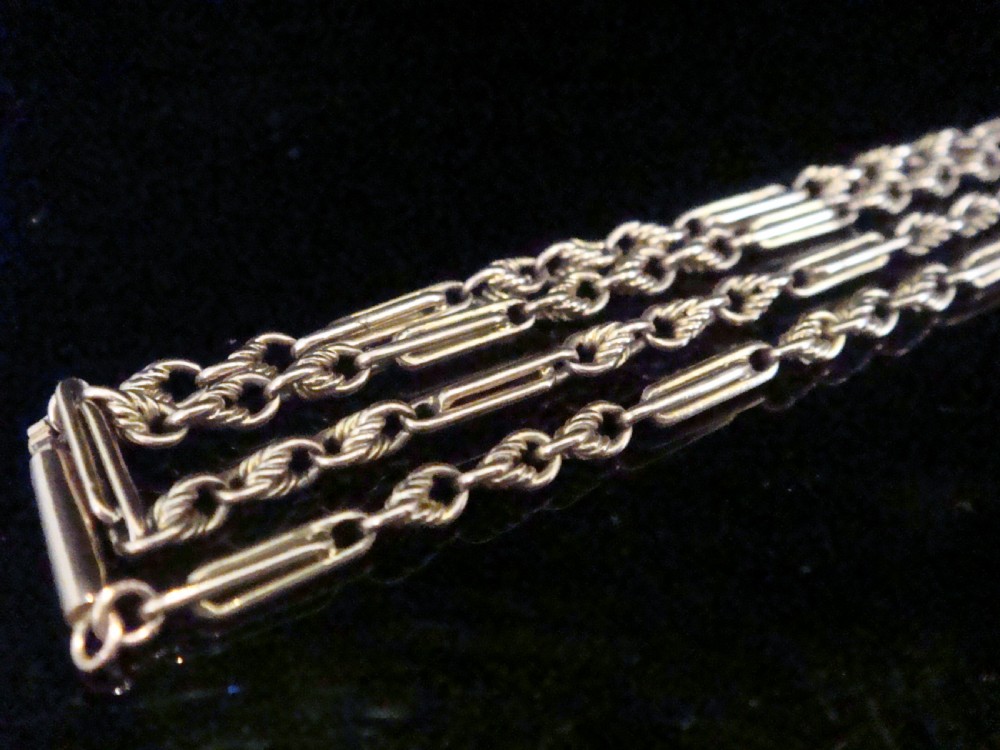 An Edwardian 9ct rose gold fetter and trombone link chain with a barrel clasp displayed on a dark surface. View II