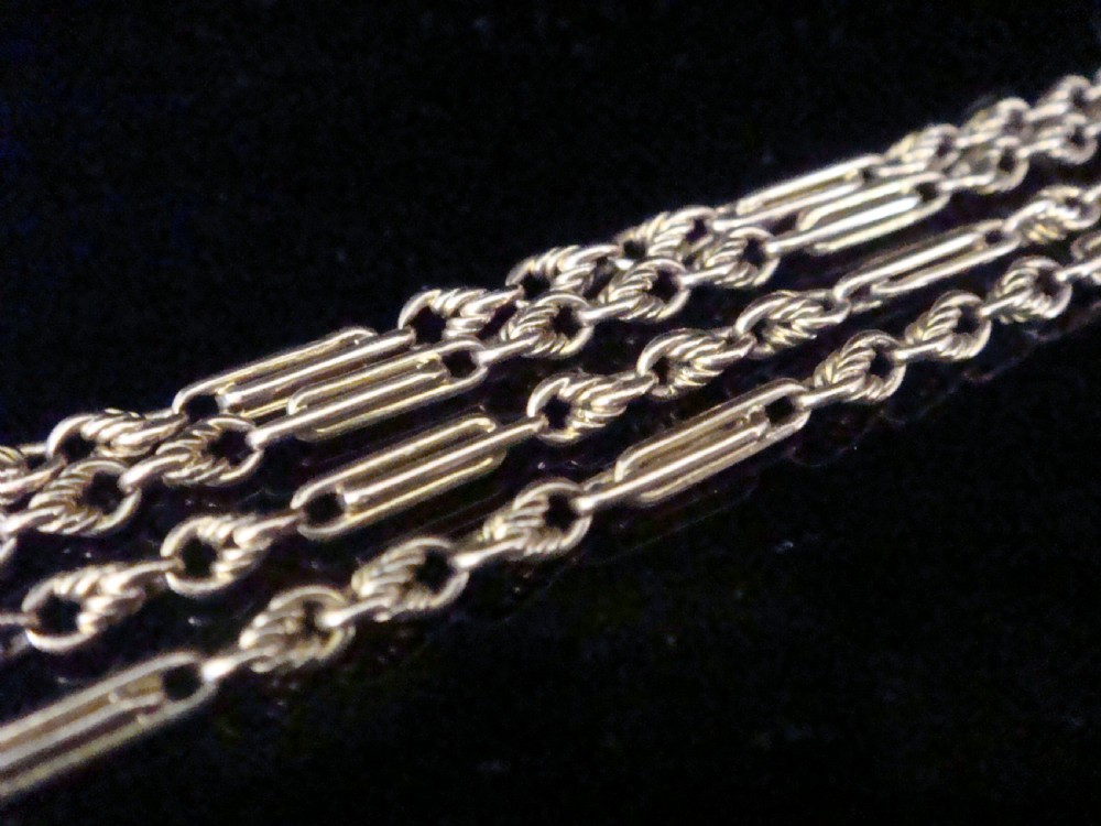 An Edwardian 9ct rose gold fetter and trombone link chain with a barrel clasp displayed on a dark surface. View III