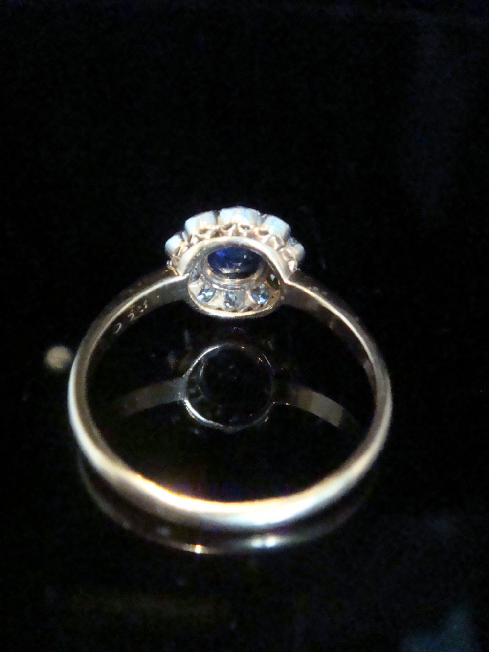 An Edwardian 18ct gold cluster ring featuring a central oval blue sapphire surrounded by a scalloped halo of small diamonds. View IV