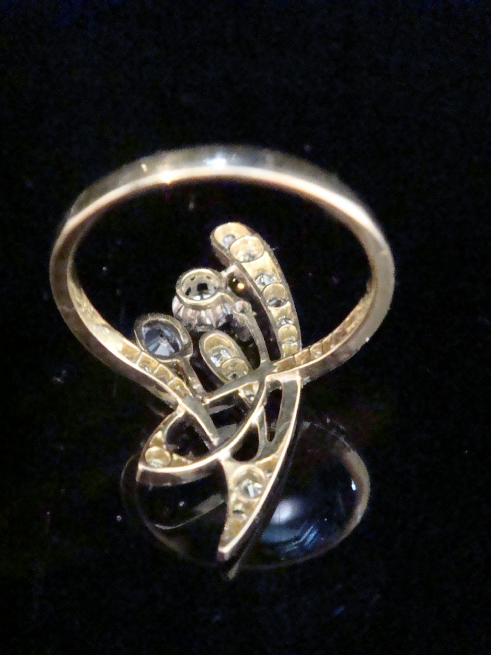 An Art Nouveau asymmetrical ring featuring fluid platinum bands encrusted with diamonds leading to a central diamond and an oval blue sapphire set in gold. View III