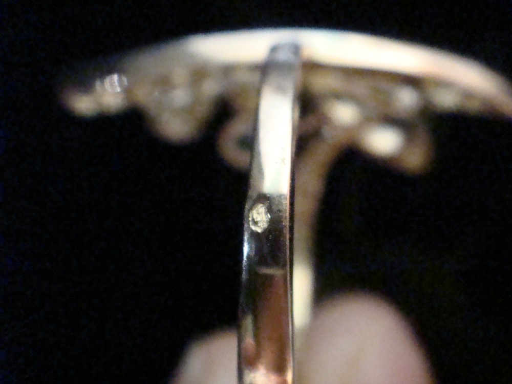 An Art Nouveau asymmetrical ring featuring fluid platinum bands encrusted with diamonds leading to a central diamond and an oval blue sapphire set in gold. View II
