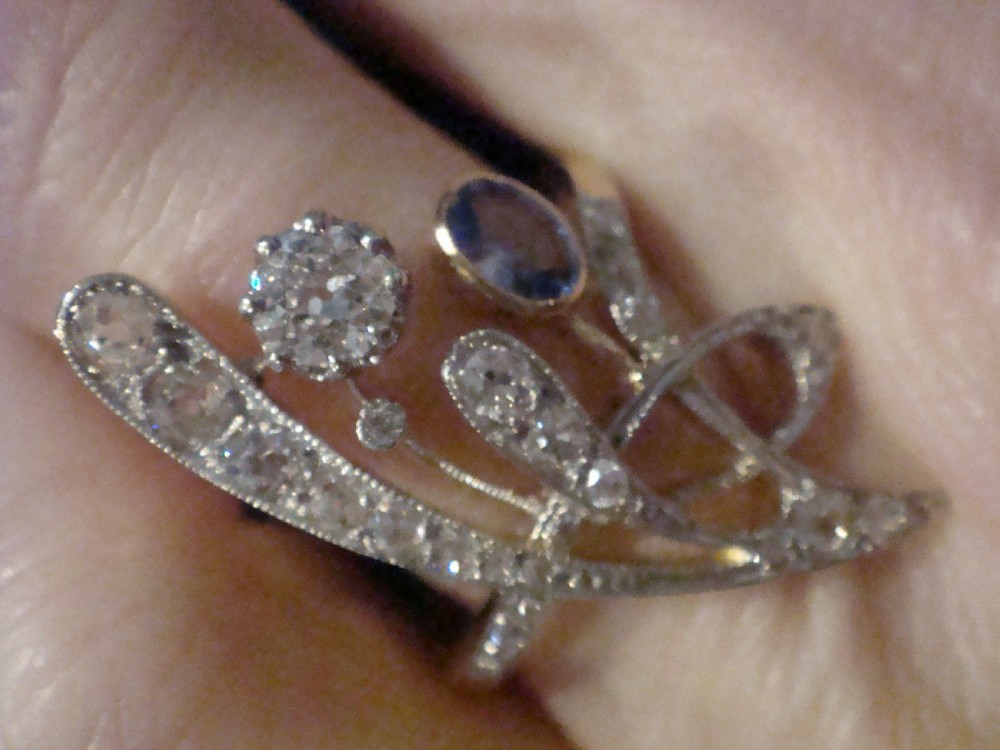 An Art Nouveau asymmetrical ring featuring fluid platinum bands encrusted with diamonds leading to a central diamond and an oval blue sapphire set in gold. View VI