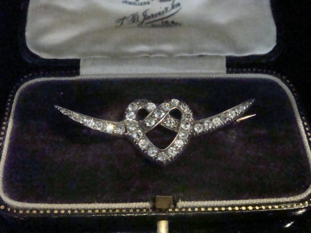 An Edwardian heart-shaped brooch set with diamonds and flanked by curved winged extensions, resting in a velvet fitted box.