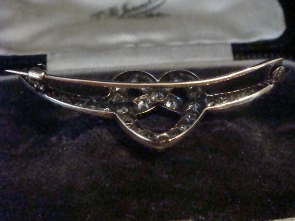 An Edwardian heart-shaped brooch set with diamonds and flanked by curved winged extensions, resting in a velvet fitted box. View V
