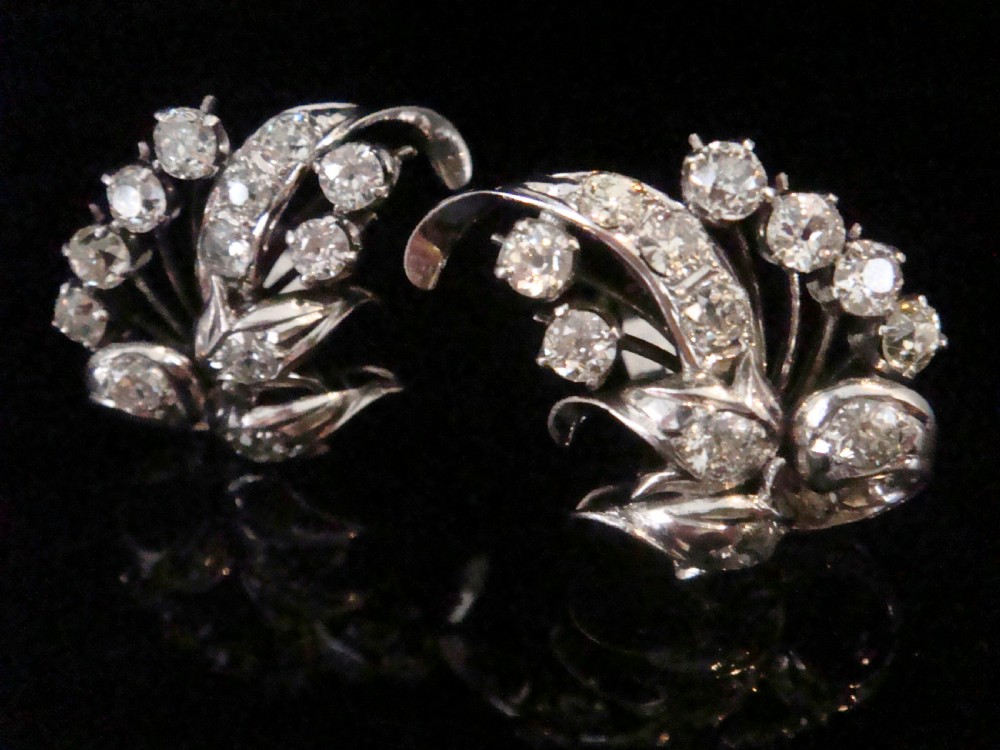 A pair of 18ct white gold cluster earrings featuring old cut diamonds arranged in a curved leaf spray design against a dark background.