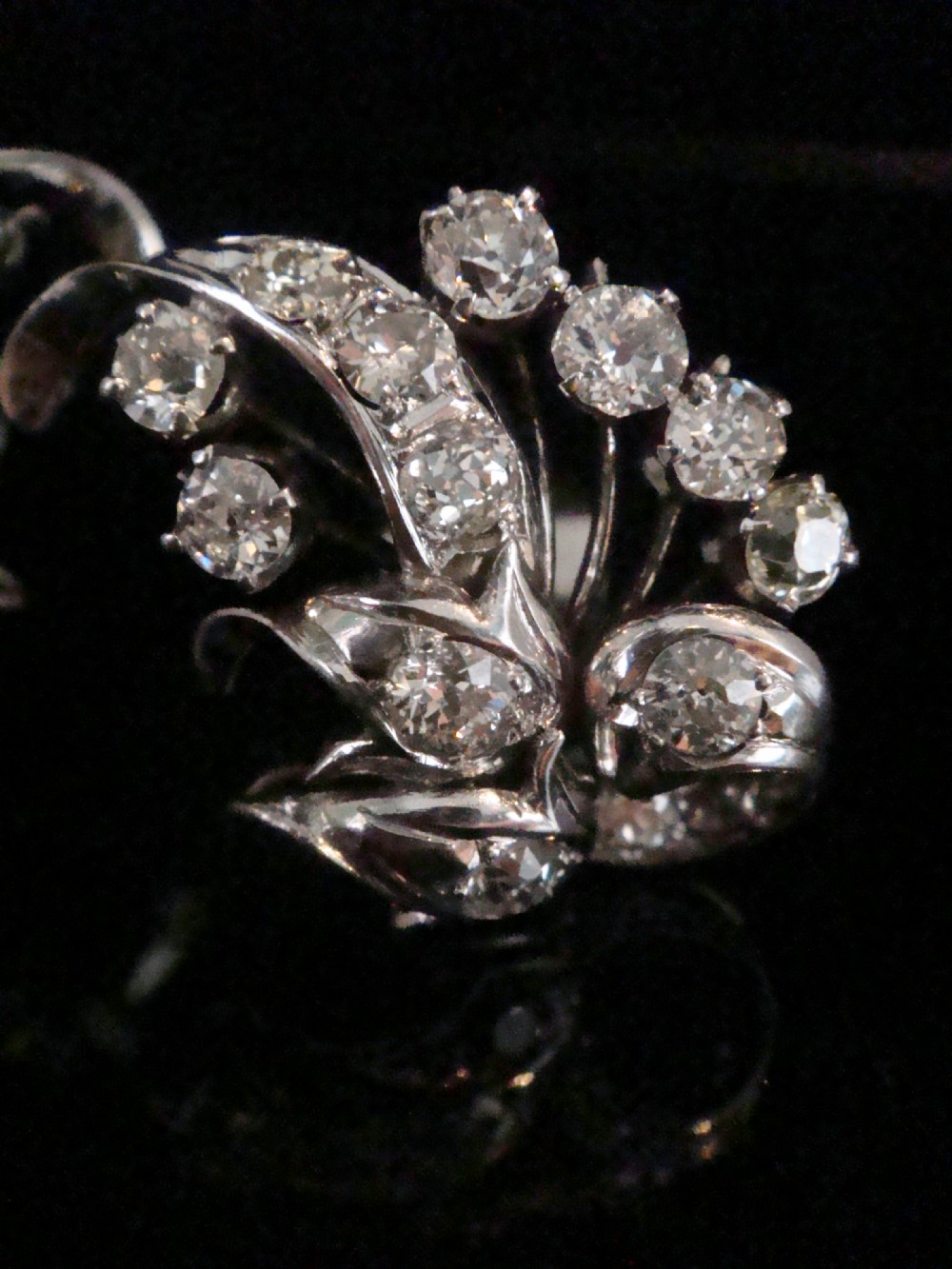 A pair of 18ct white gold cluster earrings featuring old cut diamonds arranged in a curved leaf spray design against a dark background. View II