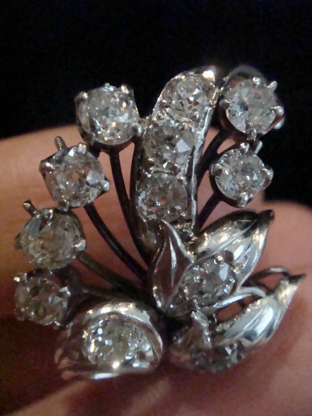 A pair of 18ct white gold cluster earrings featuring old cut diamonds arranged in a curved leaf spray design against a dark background. View IV
