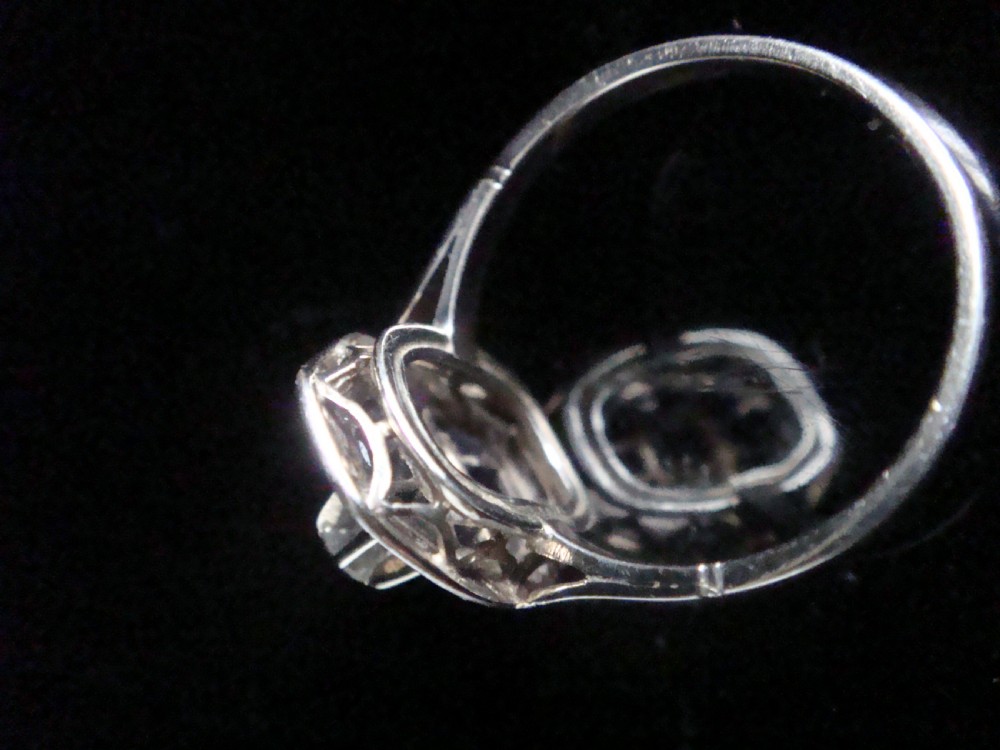 An Art Deco 18ct white gold ring featuring a central diamond encircled by dark blue calibrated sapphires and an outer geometric diamond bezel. View III