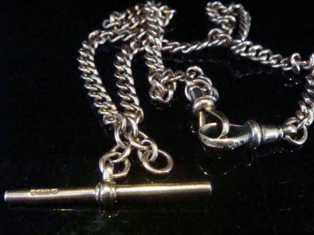 An Edwardian 9ct rose gold curb-link Albert chain featuring double dog clips and a central T-bar. View V