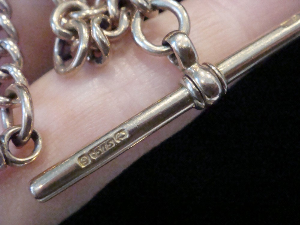 An Edwardian 9ct rose gold curb-link Albert chain featuring double dog clips and a central T-bar. View VI