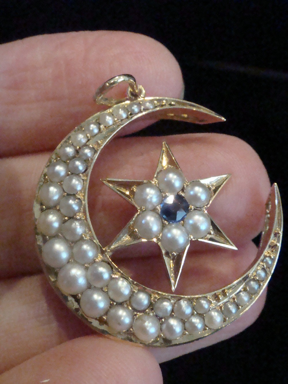 Victorian 15ct yellow gold crescent moon pendant set with split seed pearls, enclosing a central six-pointed star with a blue sapphire.