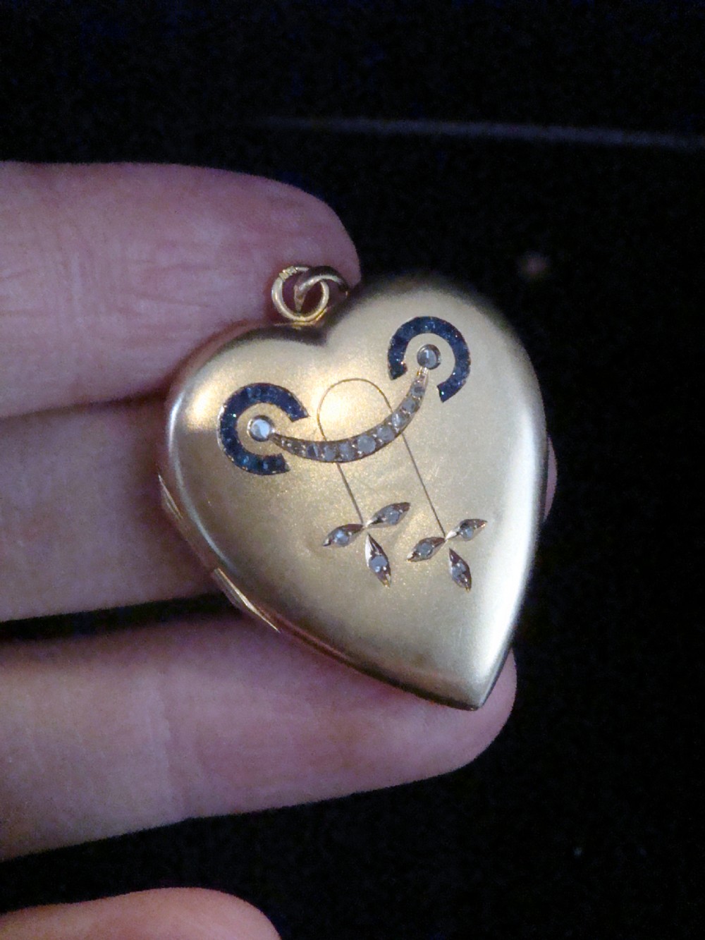 An 18ct yellow gold heart-shaped locket embellished with diamonds and sapphires in a garland pattern.