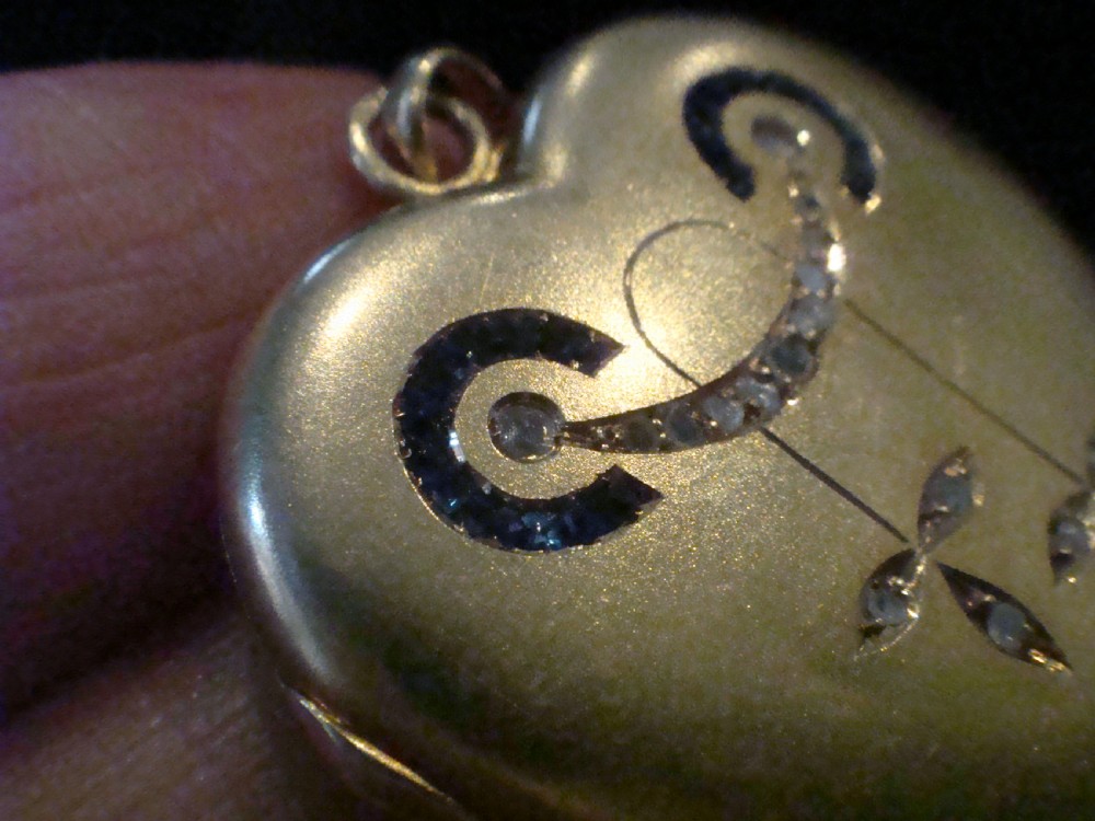 An 18ct yellow gold heart-shaped locket embellished with diamonds and sapphires in a garland pattern. View IV