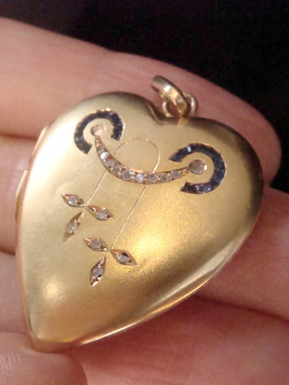 An 18ct yellow gold heart-shaped locket embellished with diamonds and sapphires in a garland pattern. View VI