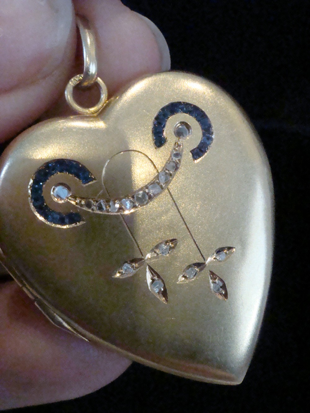 An 18ct yellow gold heart-shaped locket embellished with diamonds and sapphires in a garland pattern. View X